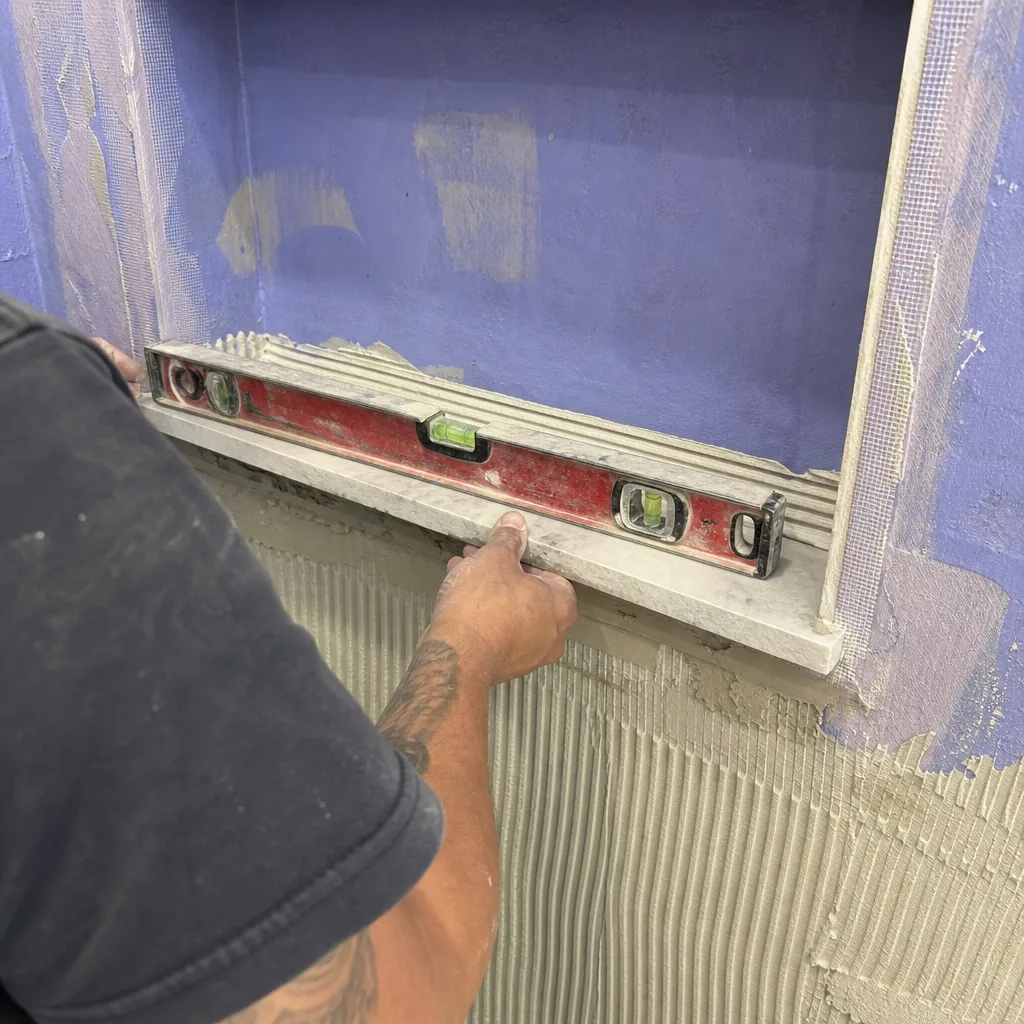 professional contractor installing a marble sill in a bathroom shower niche